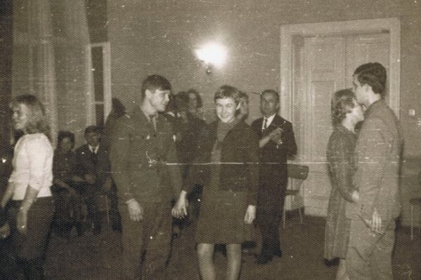 Czarno-białe zdjęcie z lat 60. przedstawiające ludzi tańczących w sali świetlicy. Na pierwszym planie para – kobieta w sukience i mężczyzna – trzymają się za ręce, obok druga para tańczy blisko siebie. W tle widać innych uczestników zabawy siedzących przy ścianie oraz stojącego mężczyznę w garniturze.