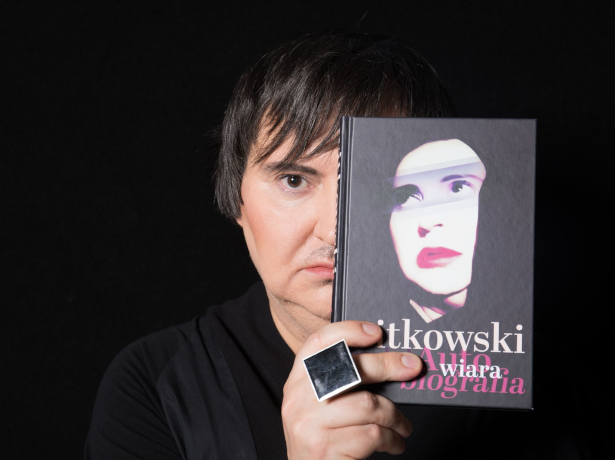 Na zdjęciu znajduje się mężczyzna, którego lewą połowę twarzy zasłania okładka książki, którą trzyma w swej prawej dłoni. Na jednym z palców ma założony duży pierścień w postaci czarnego kwadratu. Mężczyzna ma na sobie koszulę w kolorze czarnym, która zlewa się z tłem tej samej barwy.