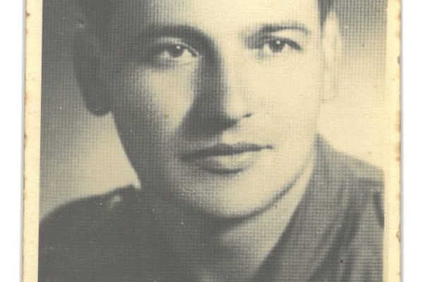 Czarno-biała, archiwalna fotografia portretowa mężczyzny – Edwarda Rewersa – przedstawionego z bliska. Ma krótko, gładko uczesane, ciemne włosy, wyraźne brwi i spokojny, poważny wyraz twarzy. Patrzy bezpośrednio w obiektyw. Ubrany jest w prostą, ciemną marynarkę lub kurtkę. Zdjęcie ma jasną, pożółkłą z wiekiem papierową ramkę z widocznymi śladami zużycia.